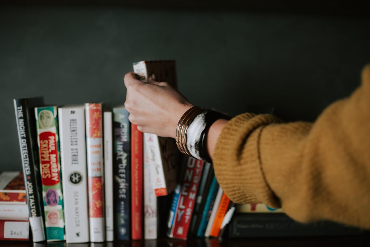 person picking a book from a bookshelf